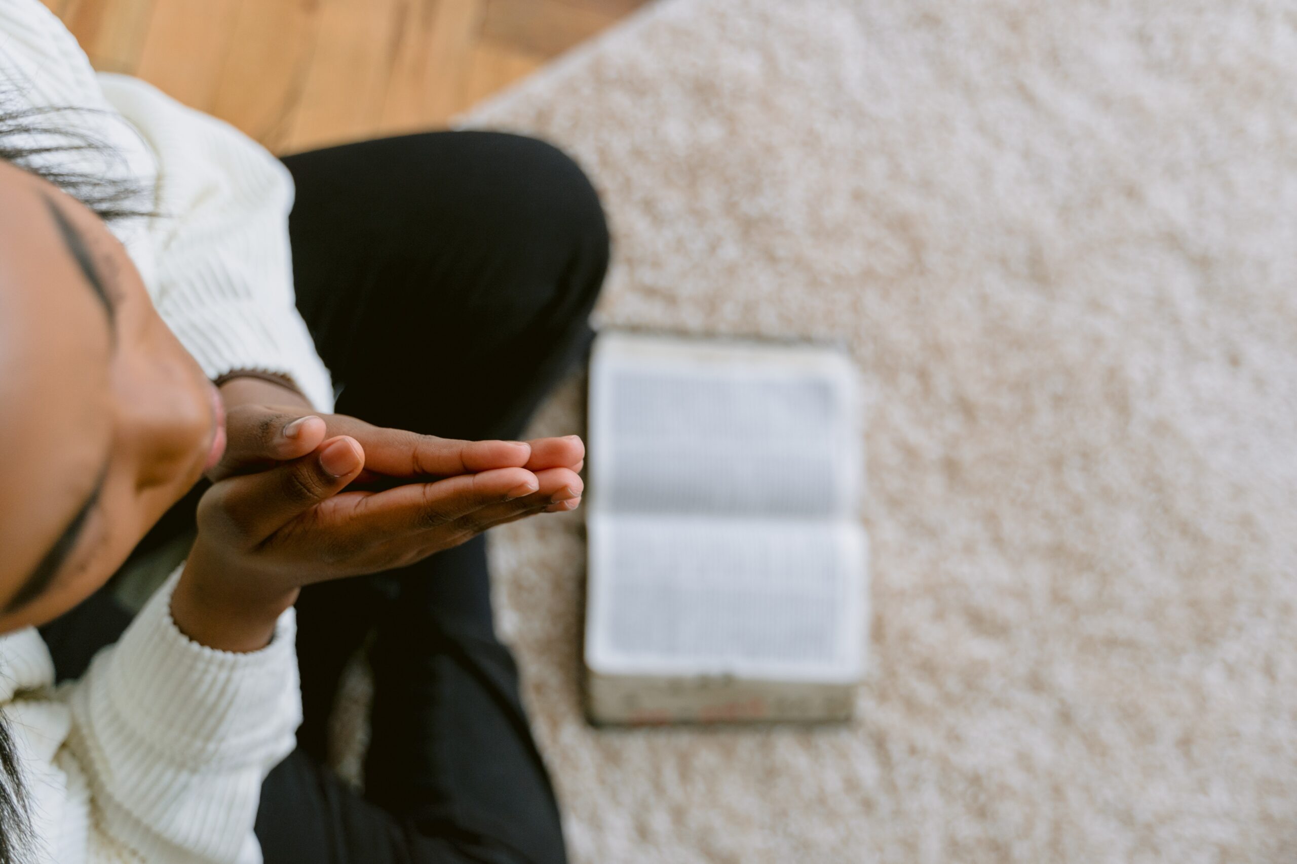 Photo a woman's hands clasped in prayer as she sits on the floor with an open Bible.