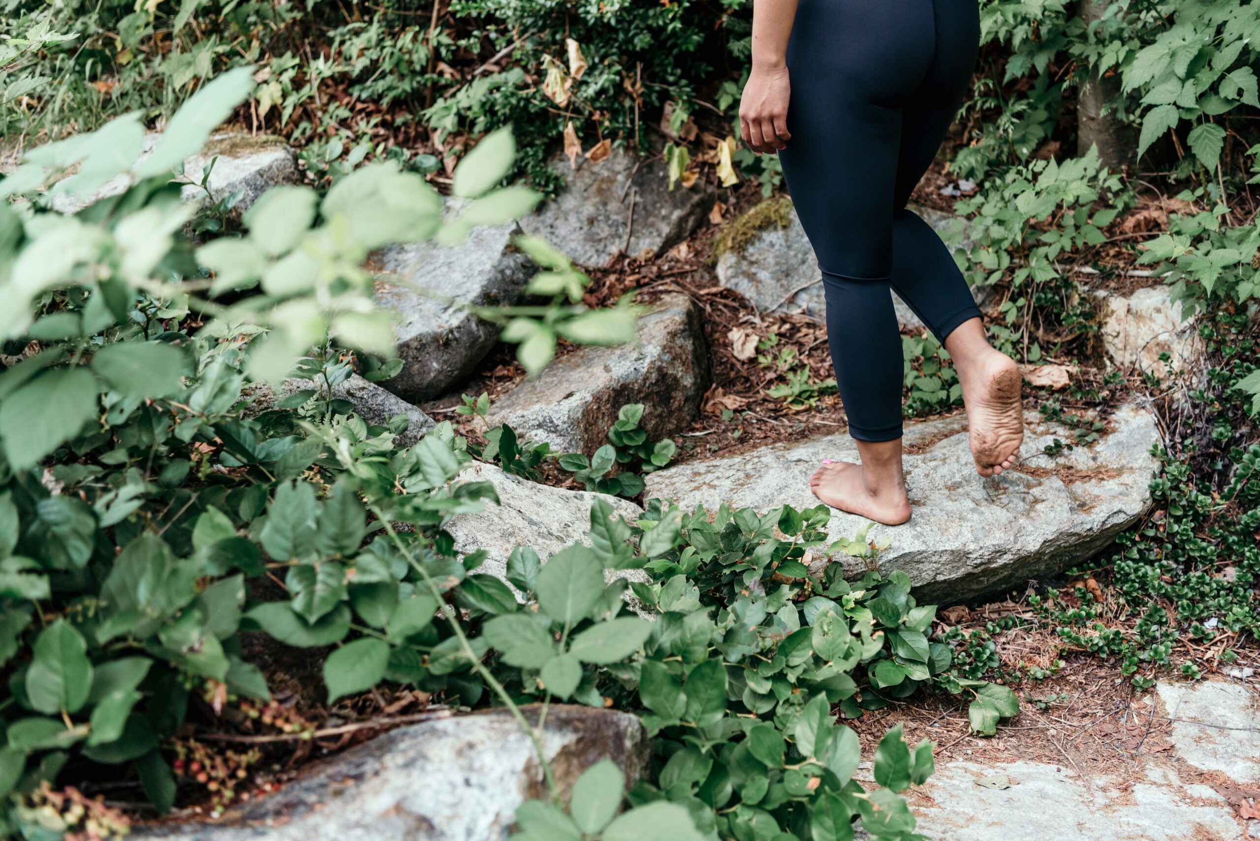woman in black leggings hiking through foliage and rocks